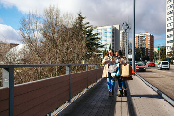 Two mature women walking, talking and using smartphone after shopping