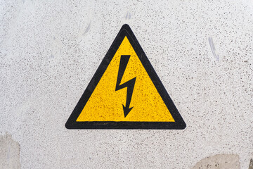 Caution sign indicating electrical hazard on concrete wall in urban setting