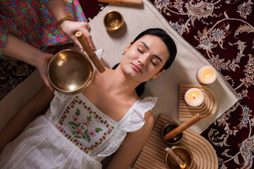 Woman undergoing singing bowl therapy indoors, top view