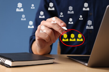 Targeting, recruitment, customer acquisition. Man circling human icons on virtual screen near laptop at table, closeup