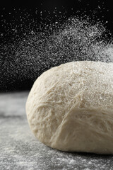 Sprinkling flour over dough on table, closeup