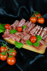 Flat lay of italian charcuterie selection on wooden board with fresh basil and cherry tomatoes, elegant food styling, catering, restaurant concept