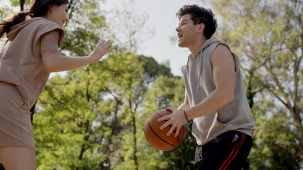 Two multiracial young people playing basketball on court at outdoors. Professional sports. Team of millennial sportsmen engaged in basketball game at outdoor court in summer. Man woman play together - Powered by Adobe