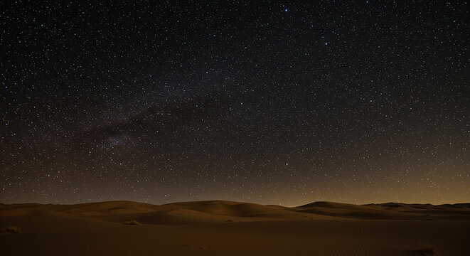 A vast desert landscape under a dark night sky filled with countless stars and a faint milky way glow above - Powered by Adobe