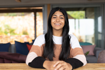 Smiling teenage girl sitting at home, wearing cozy sweater, looking confident