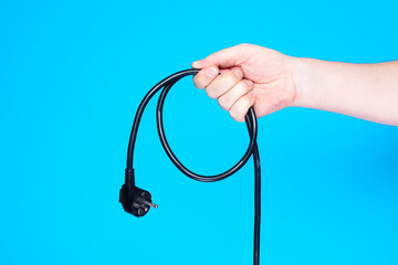 Hand holding black power cable on blue background.