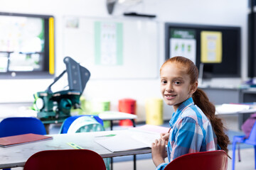 In school, smiling girl sitting at desk in classroom, ready for learning, copy space