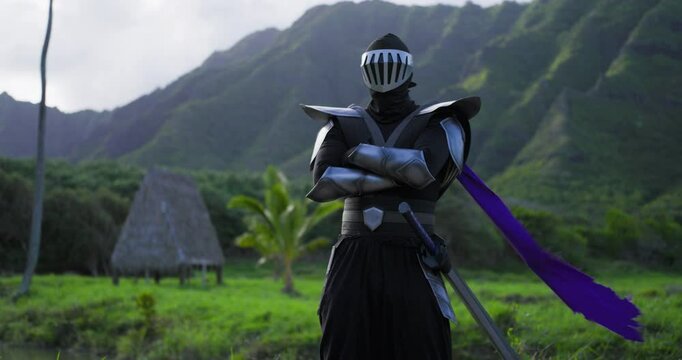 Slow dolly in on epic ninja knight standing in tropical paradise as his purple scarf blows in the wind