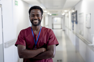 Obraz premium Confident male nurse in scrubs smiling in hospital corridor, arms crossed