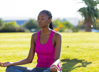 African American woman meditating on grass in backyard, enjoying peaceful moment