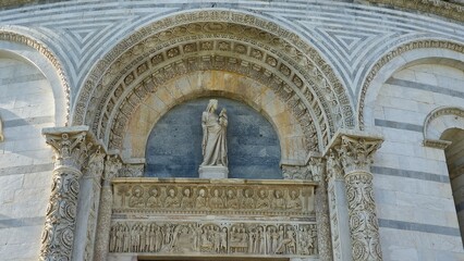 Pisa, Italy - December 30 2024. Ornate church portal with striped marble arches, intricate carvings, and a central statue of the Madonna and Child above detailed biblical reliefs.