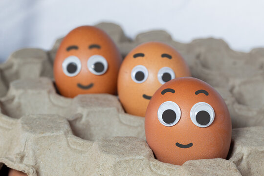Three eggs with smiling faces in a recycled cardboard box...Group of eggs with friendly expressions. National egg day concept. Creative representation of personified eggs in eco-friendly packaging.