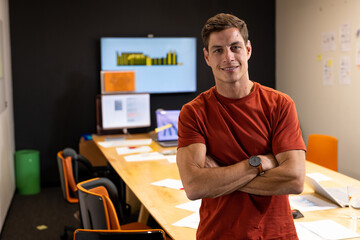 Confident man in office standing with arms crossed, smiling at camera