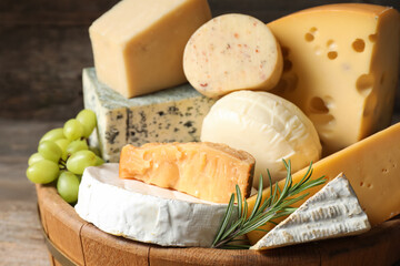Different types of cheese, rosemary and grapes in wooden tray on table, closeup