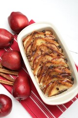 Delicious bread pudding in baking dish and fresh apples on white wooden table, flat lay
