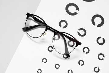 Glasses and vision test chart on gray background, top view
