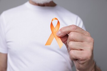 Multiple Sclerosis awareness. Senior man with orange ribbon on grey background, closeup