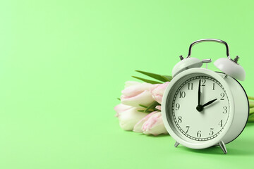 Spring time. Alarm clock and beautiful tulips on green background, space for text