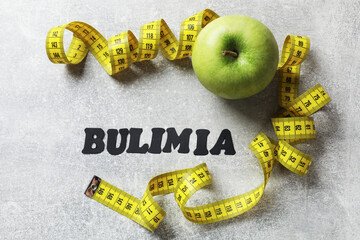 Word Bulimia, green apple and measuring tape on grey table, flat lay