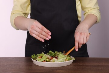 Woman salting tasty salad at wooden table against white background, closeup