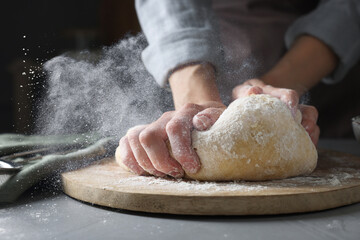 Woman kneading dough at grey table, closeup. Cloud of flour