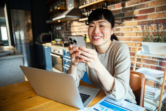 Focused Asian woman managing finances and bills at home with laptop