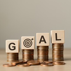 a target icon representing financial planning, Wooden blocks spelling "GOAL" rest on stacks of coins, with savings, Financial Goals and Savings Concept. achieving monetary objectives, business growth,