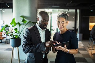 Smiling business professionals discussing project on tablet in modern office