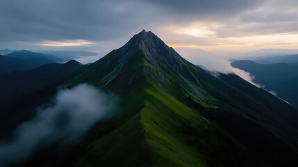 Obraz premium Majestic green mountain peak rising above low clouds during a dramatic sunrise.