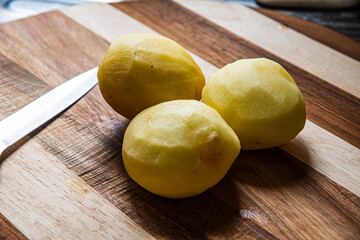 three peeled potatoes lie on a kitchen board