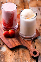 Vanilla and Strawberry Milkshakes served in glass mugs on a wooden board Features ice cream and strawberries side view of Delicious and refreshing sweet drinks