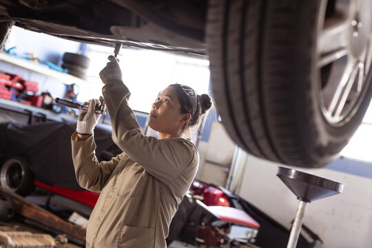Female mechanic repairing car undercarriage in garage, focusing on work
