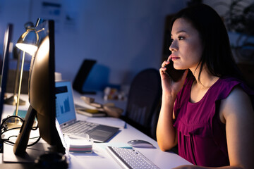Businesswoman working late at office, analyzing data on computer and phone call