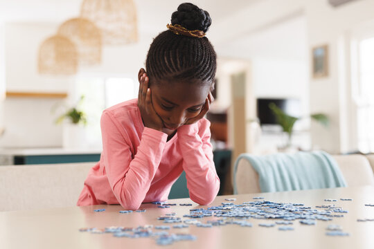 Young girl concentrating on solving puzzle pieces at home, deep in thought