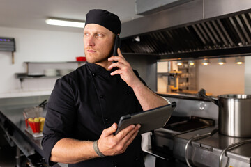 Chef in kitchen using tablet and phone, managing culinary tasks efficiently