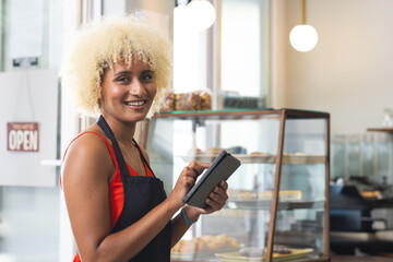 Smiling barista taking order on tablet in cozy cafe with pastries displayed
