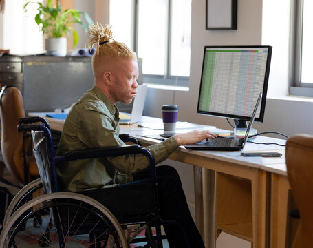 Man in wheelchair working on laptop at office desk, analyzing data spreadsheets