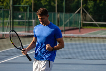 Tennis player celebrating victory on court with fist pump and racket