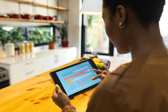 African American woman using tablet to monitor energy usage in modern kitchen