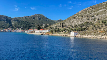 Fototapeta premium Scenic View Of Kastellorizo Island In Greece, Coastal Village With Colorful Houses, Clear Blue Sea, Rocky Hills, And Bright Sky, Peaceful Summer Destination, Ideal For Travel, Tourism, And Getaways.