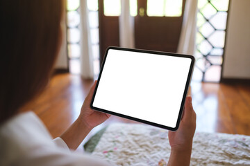 Mockup image of a woman holding tablet with blank desktop white screen on the bed at home