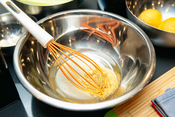 Whisking ingredients in stainless steel mixing bowl. A stainless steel mixing bowl with a whisk and liquid ingredients, likely for baking or cooking, placed on a kitchen countertop with lemons nearby.