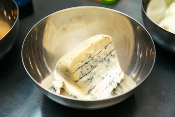 Blue cheese wedge in stainless steel bowl. A creamy wedge of blue cheese with marbled veins of...