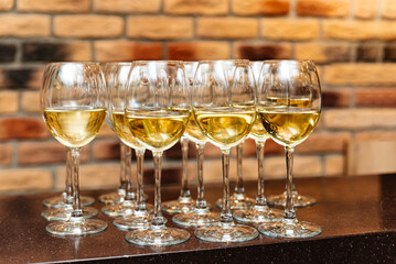 Glasses of white wine on a bar counter. A collection of elegant wine glasses filled with white wine, arranged on a bar counter against a rustic brick wall background.