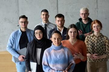 A diverse and determined team of business professionals stands confidently in an office, ready to...