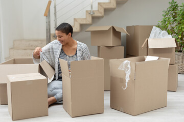 Smiling woman unpacking cardboard boxes at home, enjoying new living space, copy space