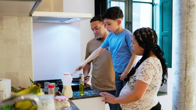 Latin family cooking together in modern kitchen, pregnant mom teaching son to cook while dad watches
