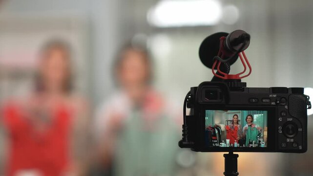 Rear view behide camera screen display two women influencer shoot vlog video review clothes prim social media or blog. Girls with apparel studio lighting for live streaming marketing recording session