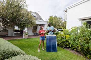 Diverse couple discussing solar panel installation in garden, enjoying sustainable living
