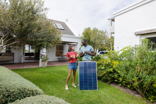 Diverse couple discussing solar panel installation in garden, enjoying sustainable living - Powered by Adobe